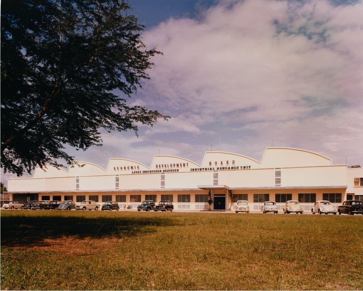 A long, low modernist building with a saw-tooth roofline, lettered “Economic Development Board — Light Industries Services — Industrial Research Unit”, with 1960s cars parked in front.